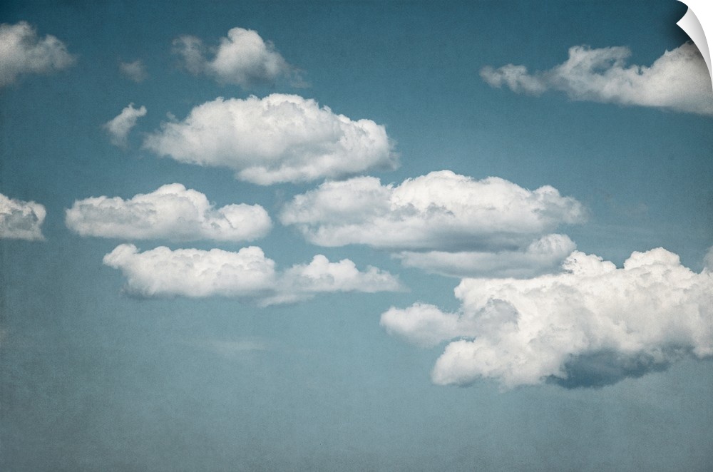 A contemporary photograph of fluffy white clouds against a pale blue sky.