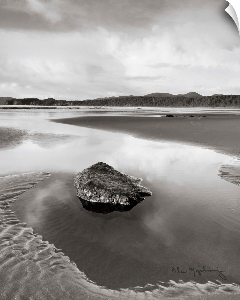 A black and white photograph of an idyllic beach scene, with a large rock in the foreground.