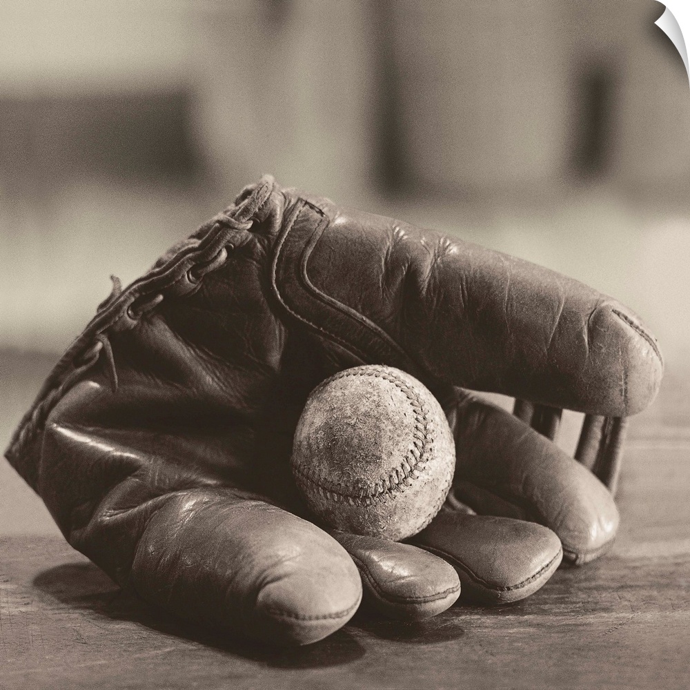 Square sepia toned photograph of a worn baseball in a vintage mitt on a soft focus backdrop.