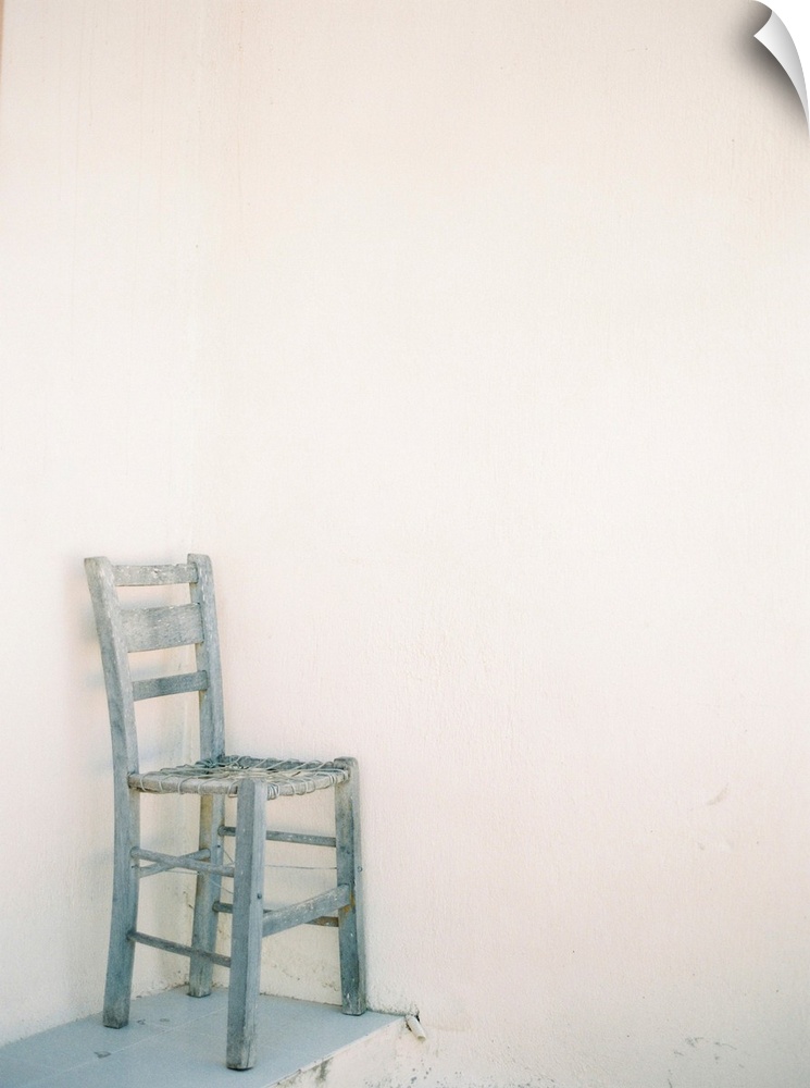 A photograph of a very rustic wooden and rope chair on a ledge in front of a mediterranean building.