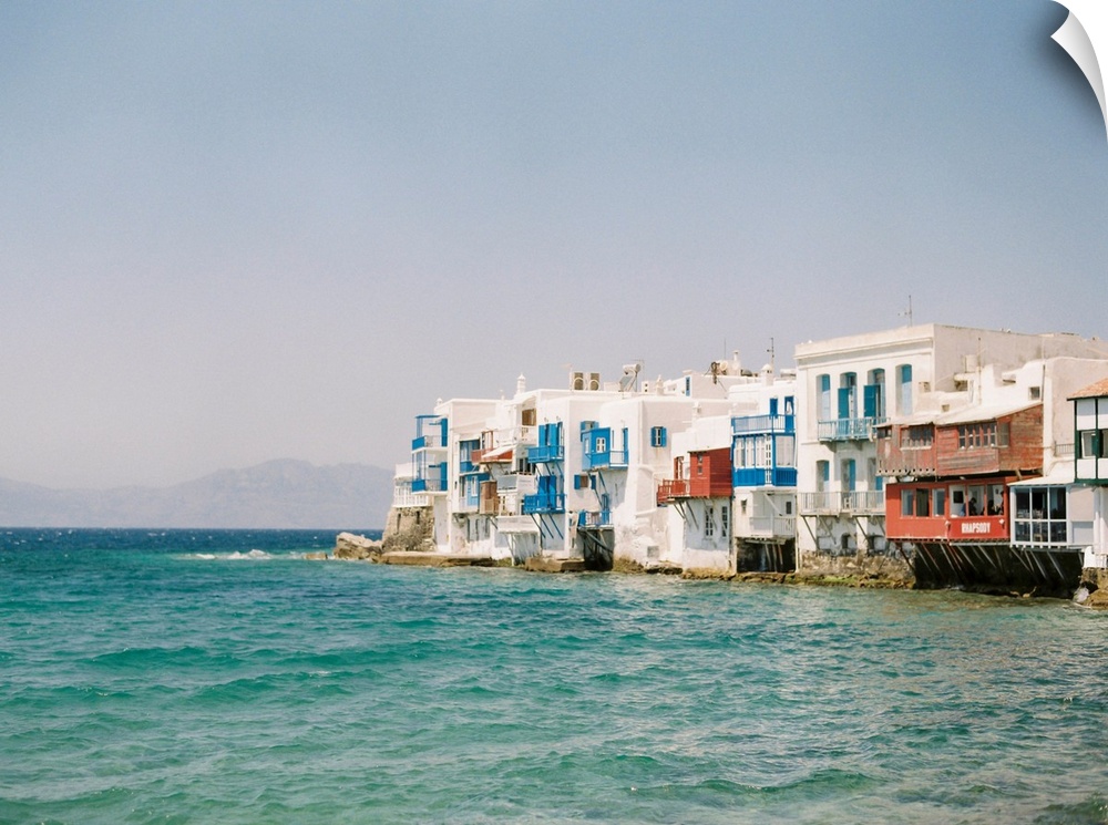 Photograph of white buildings with colorful balconies overlooking the water in Mykonos, Greece.