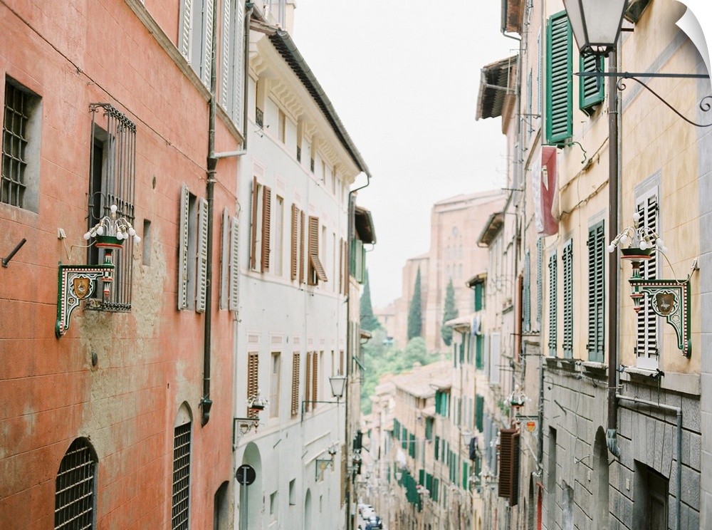 Photograph of a narrow alleyway between two tall buildings adorned with shutters, Italy.