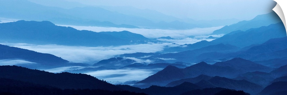 Panoramic landscape photograph of blue mountains covered in fog.