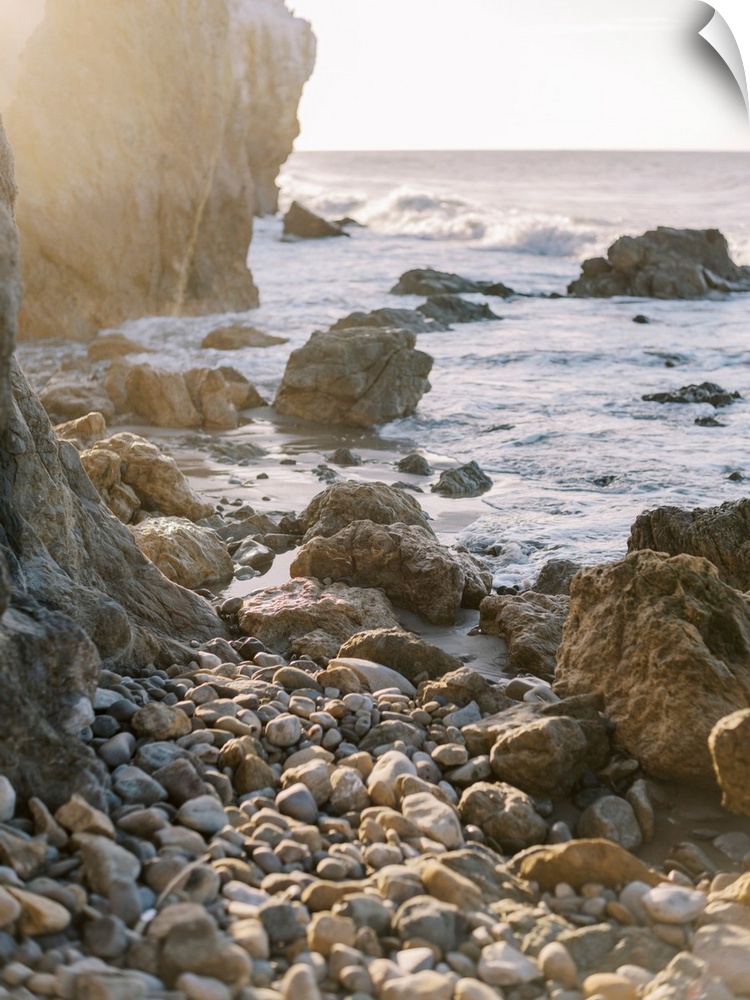 A photograph of rocks and boulders at the edge of a rugged coastline at sunset.