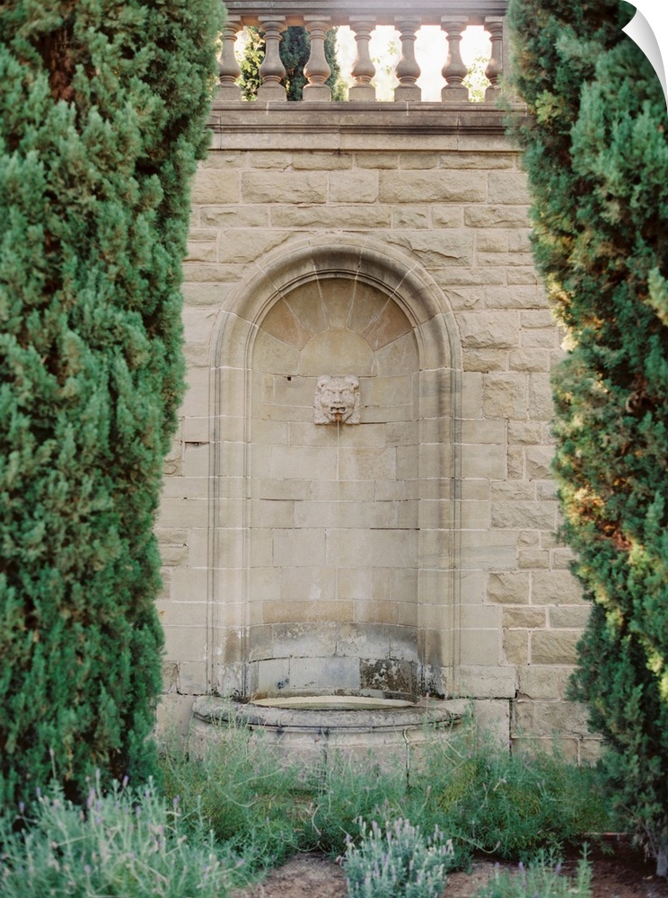 A photograph of an ornate fountain set into the wall amidst elegant gardens of a Mediterranean villa.