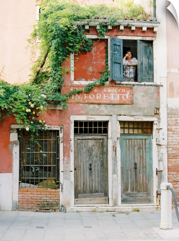 Photograph of a woman looking out of the window of a very old building, Venice, Italy.