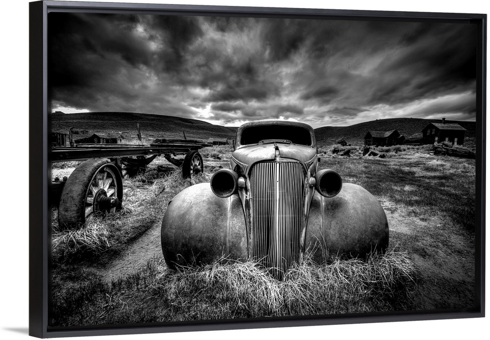 A black and white photograph of derelict vintage car sitting in a desert landscape.