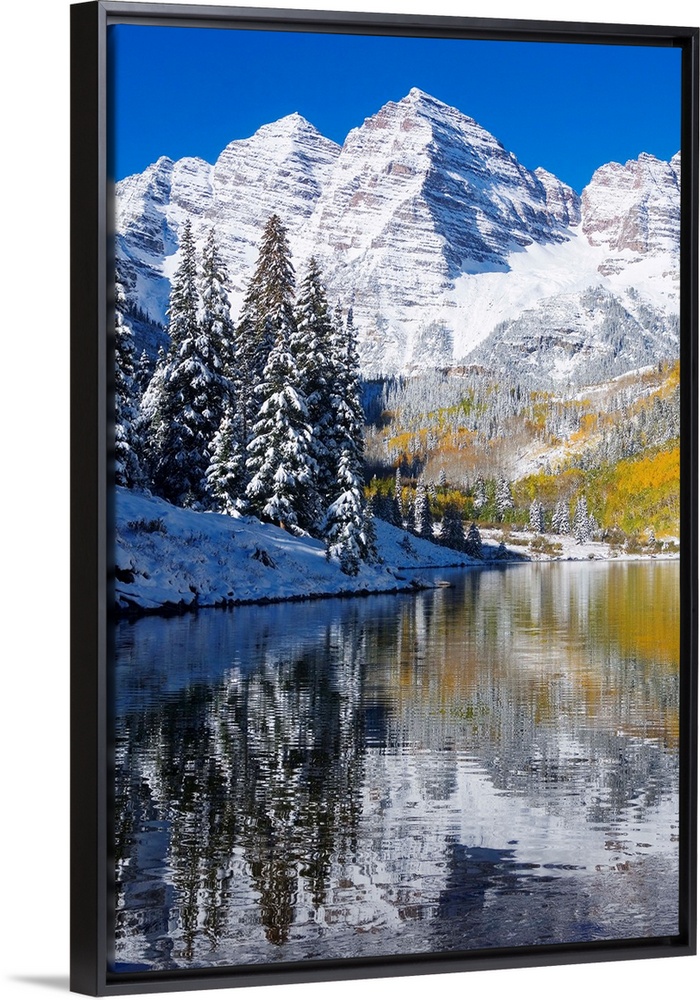 Snow covered mountains are pictured against a clear blue background that reflects down in the body of water that is in the...