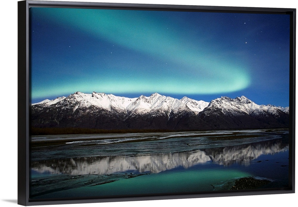 A landscape photograph of the aurora borealis and mountains reflecting in a lake filled with ice.