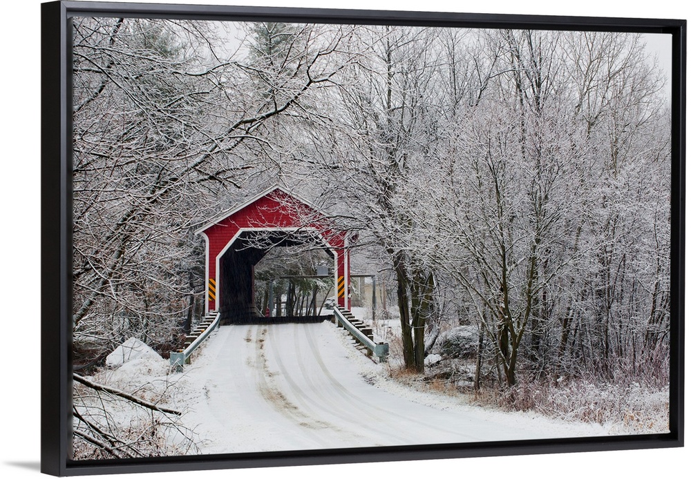 Snow covered trees surround a road that leads up to a covered bridge.