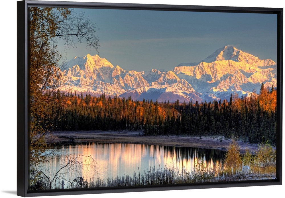 Serene landscape at dawn of two snow-covered mountains near a pine forest at the edge of a small pond in Alaska.