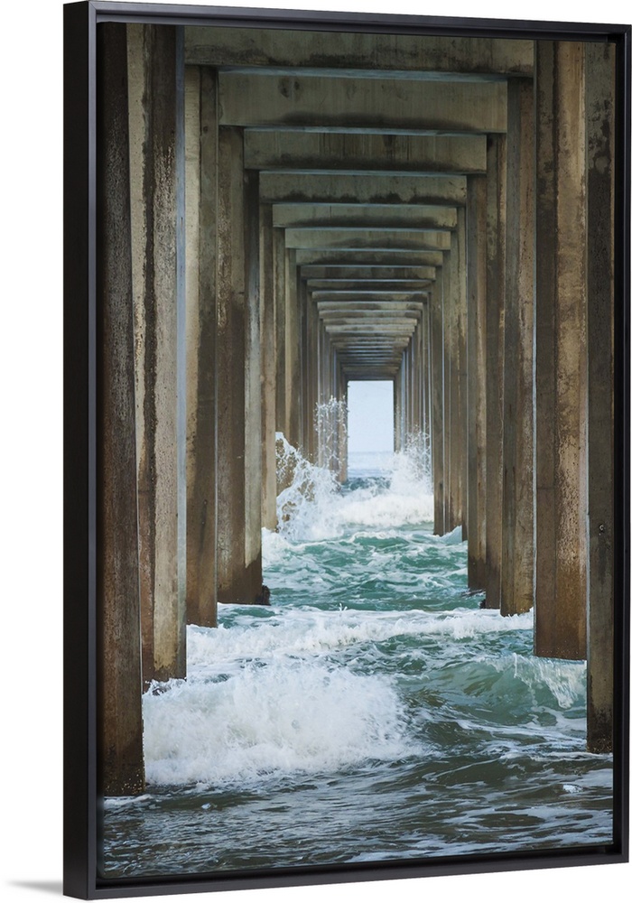 Photograph under a large pier looking out into the distance at the blue water.