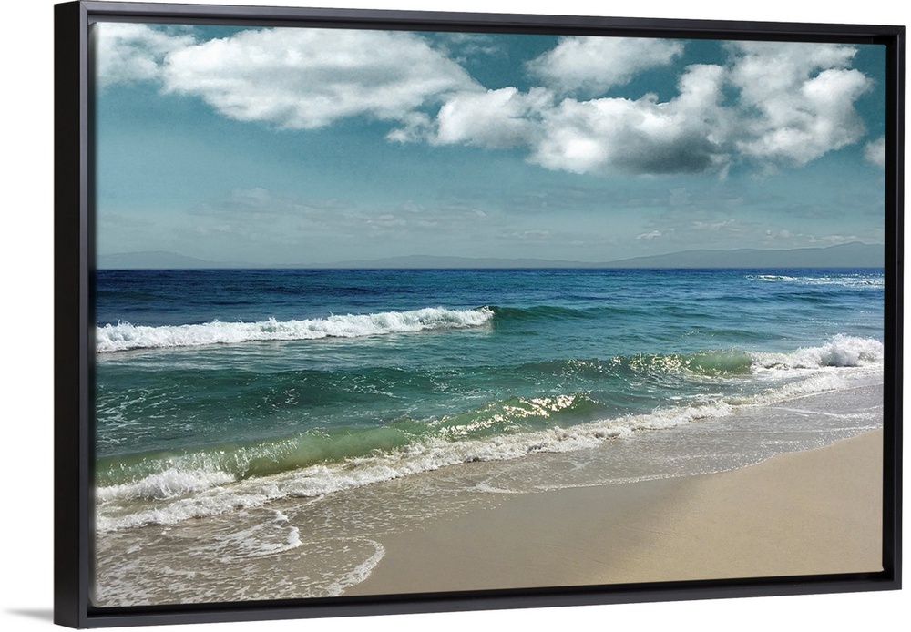 This serene photo shows rippling waves as they approach the beach with puffy white clouds in the background.