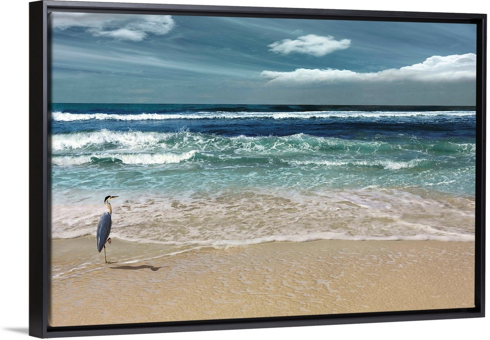 This serene photo shows rippling waves as they approach the heron on the beach with white clouds in the background.