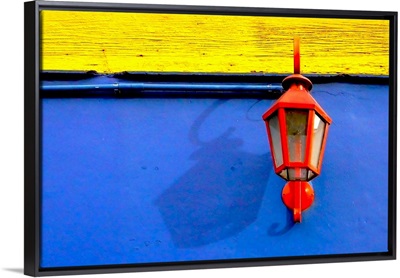 A red streetlamp on a blue and yellow wall.