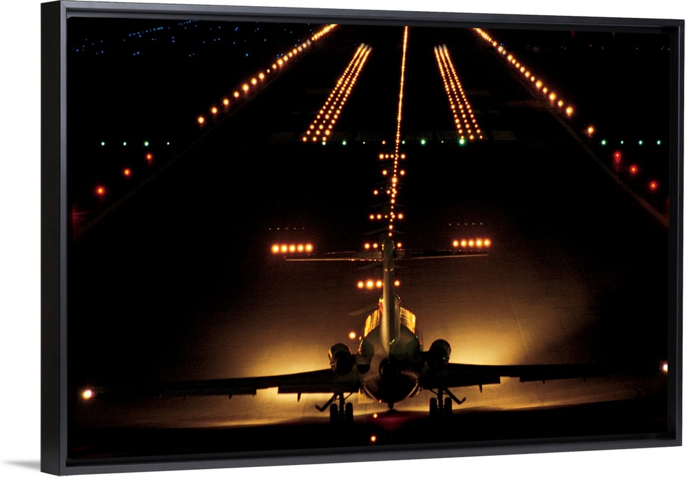 Giant photograph shows a small aircraft stationed at the end of a brightly lit airstrip at nighttime.
