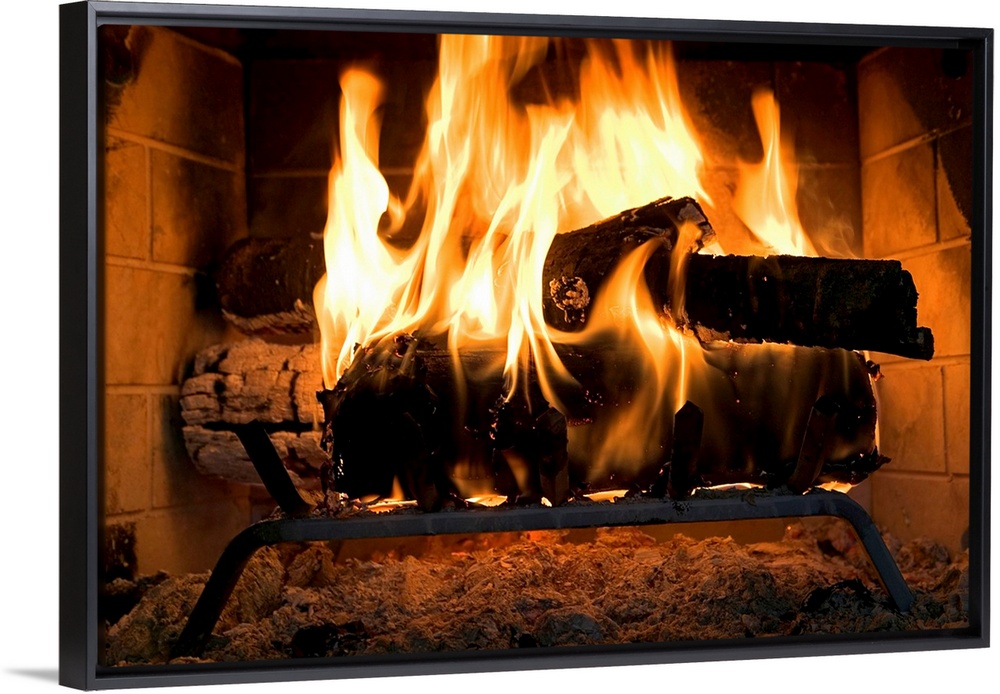 A horizontal photograph of logs burning inside a personal, home fireplace lined with bricks