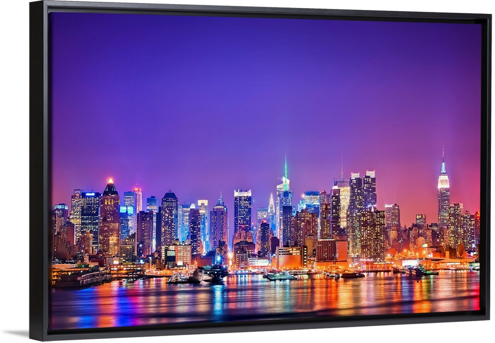 Photograph of New York skyline at night with the Hudson River in foreground.  The building lights are reflected in the water.