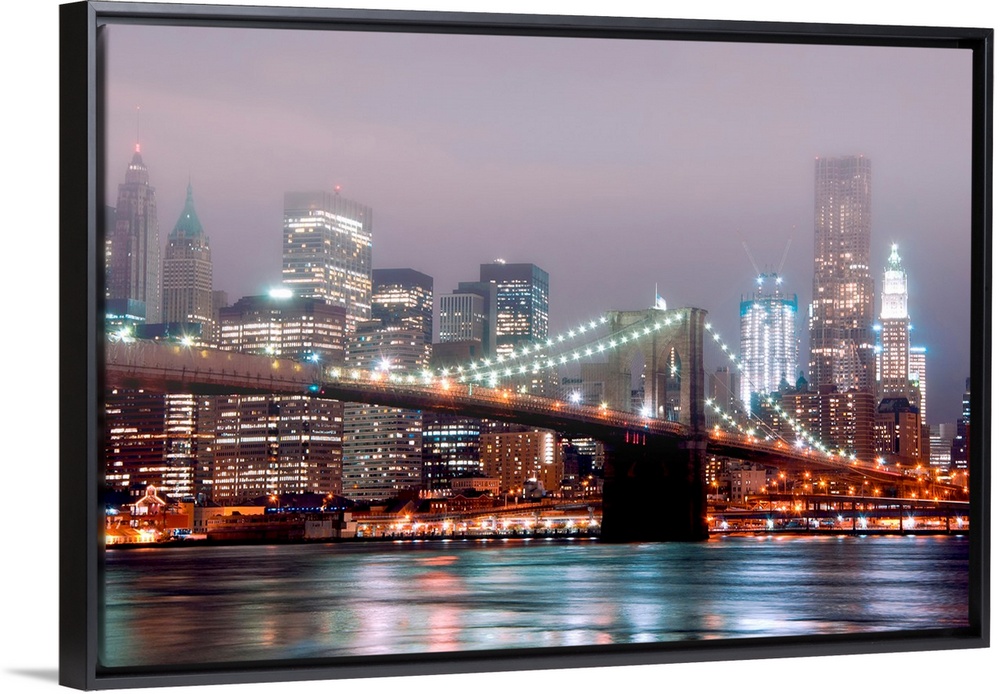 A misty night scene illuminated by urban lights of downtown Manhattan photographed from the Brooklyn shore.