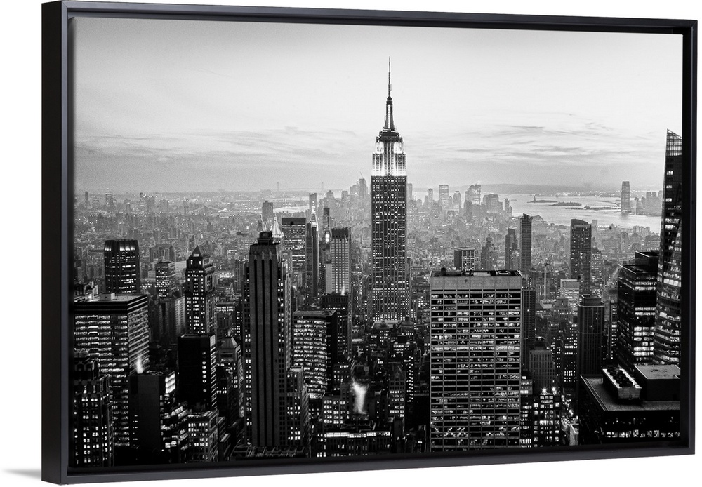 High angled photograph of city buildings at dusk.  The building windows are filled with light creating little rectangle pa...