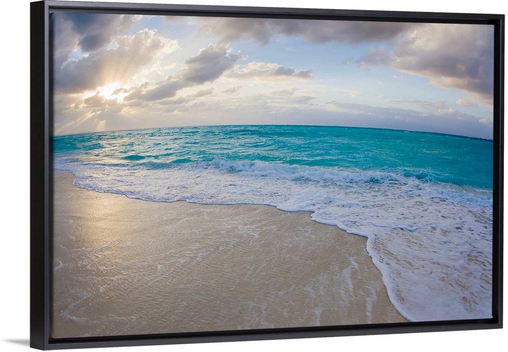 From the National Geographic Collection a wide angle photograph of the sun setting behind clouds while waves washed up aga...