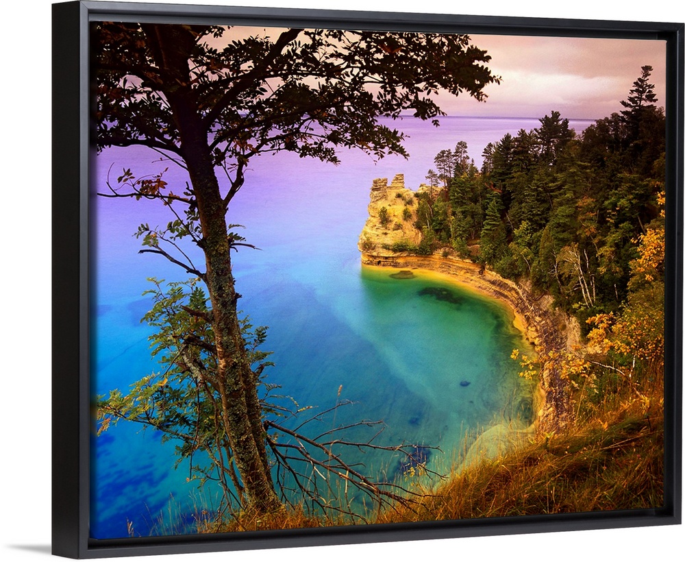 An immense cliff is covered with various trees and thick foliage that curves and overlooks Lake Superior.