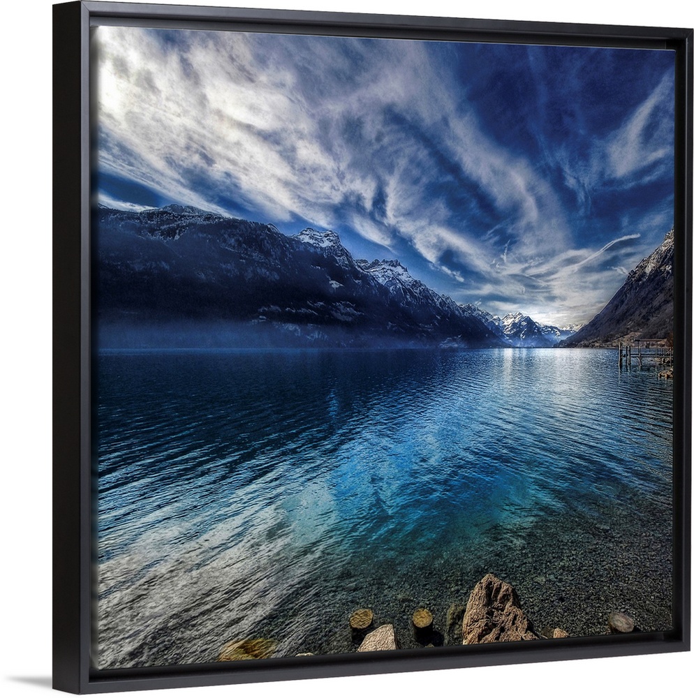This square shaped decorative wall art is a landscape photograph of a lake surrounded by snow covered mountains beneath a ...