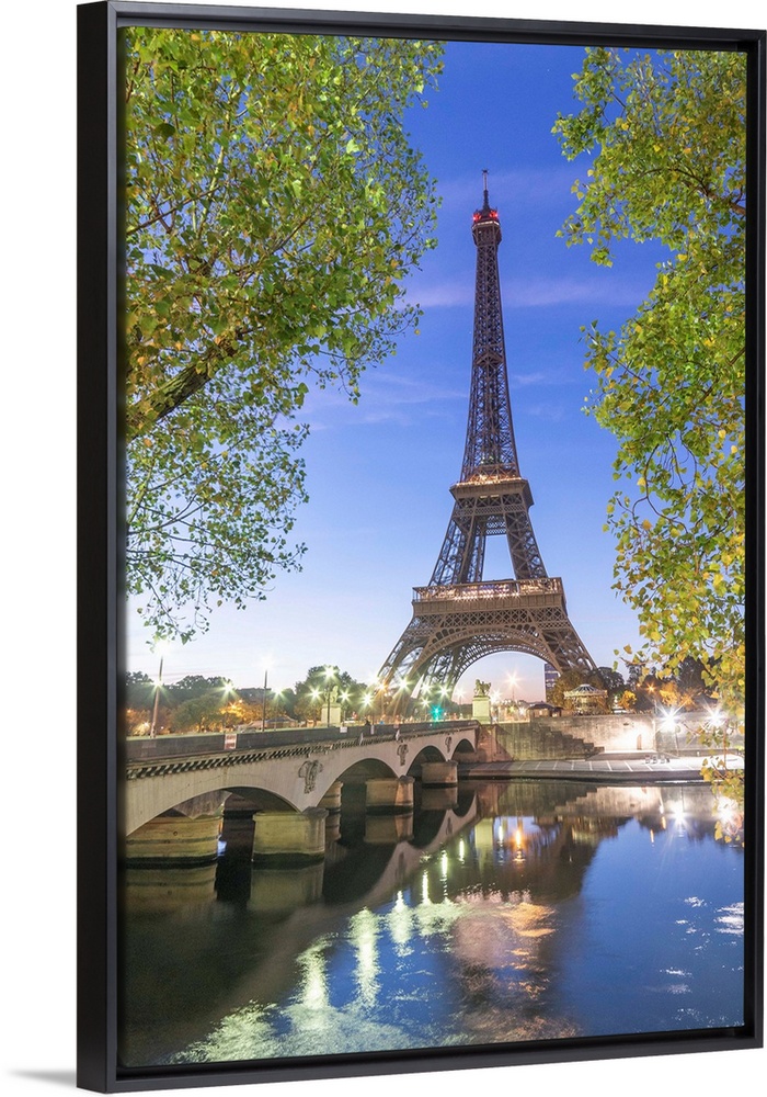 Early morning for the Eiffel tower in Paris, facing the Jena bridge with green trees around and lights.