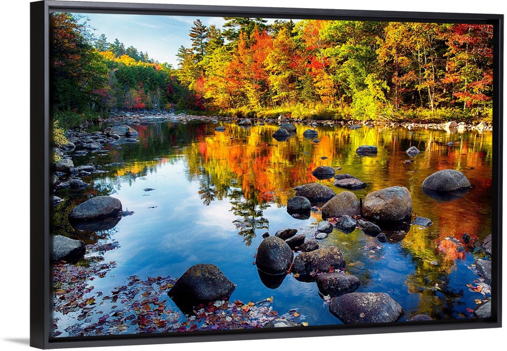 Fine art photo of bright colors of a forest in autumn being reflected in a pond full of rocks.