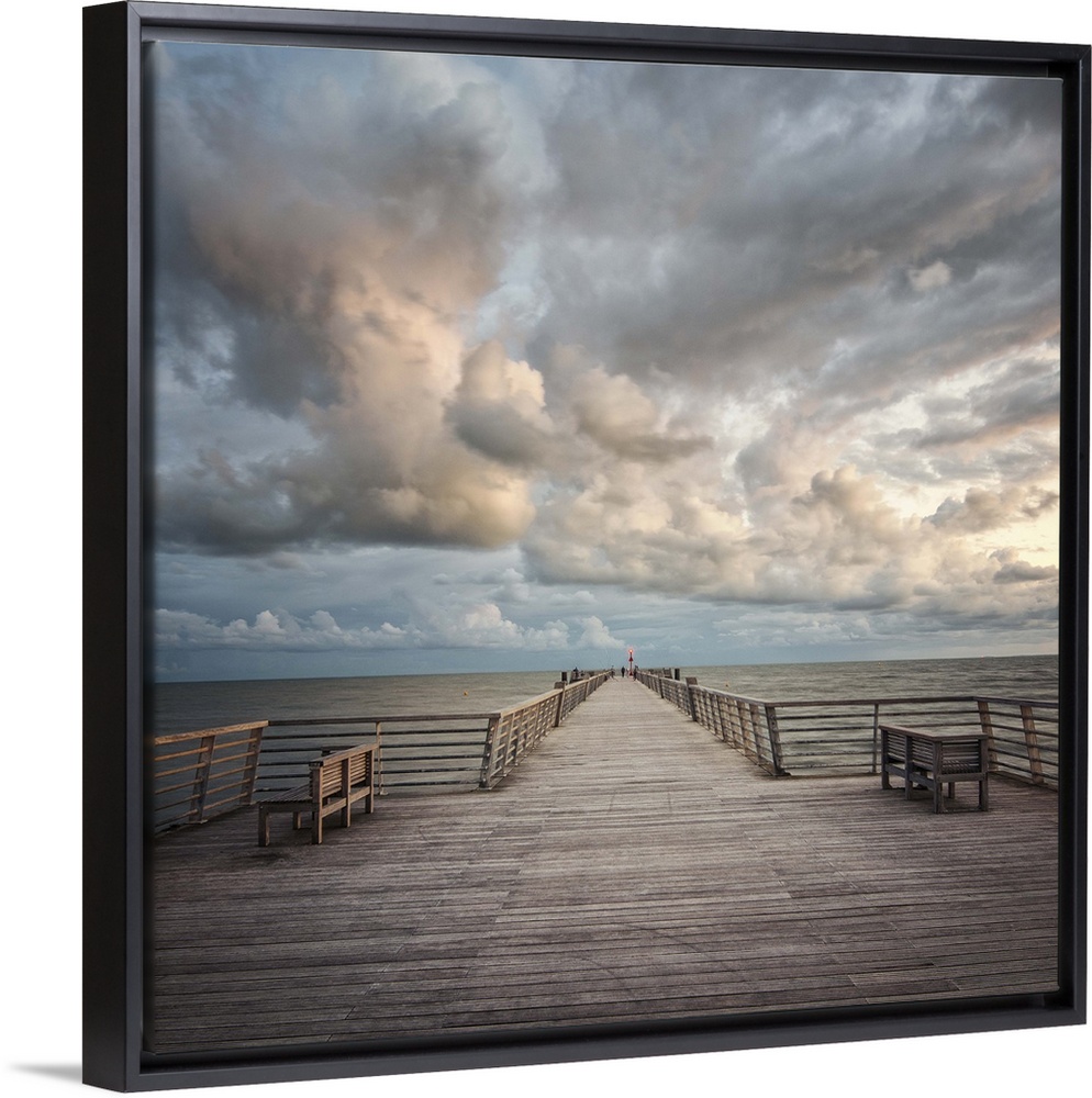 A wooden pier leading to the ocean with dramatic clouds above.