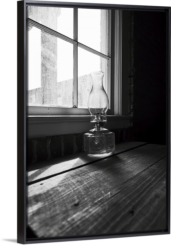 Low angle view of an old glass oil lamp on a wooden desk at a house window.