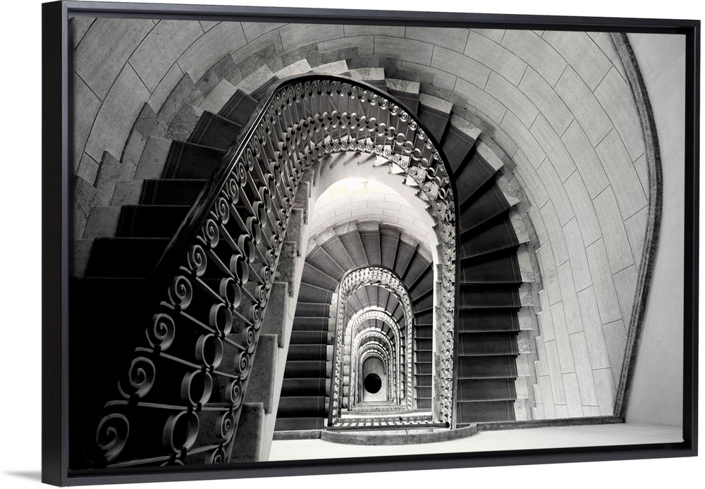 This architectural photograph looks down a historic stairwell lined with tile and iron work banister.