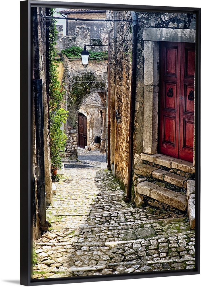 Cobblestone street in Sermoneta, Italy, with a red door on the side.