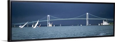 A storm approaches sailboats racing past Rose Island lighthouse and the Newport Bridge in Narragansett Bay, Newport, Rhode Island USA