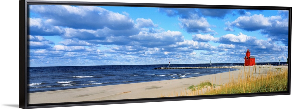 Panoramic photograph of a large lighthouse next to a dock on a sandy beach in Holland, Michigan during a sunny day.  The w...