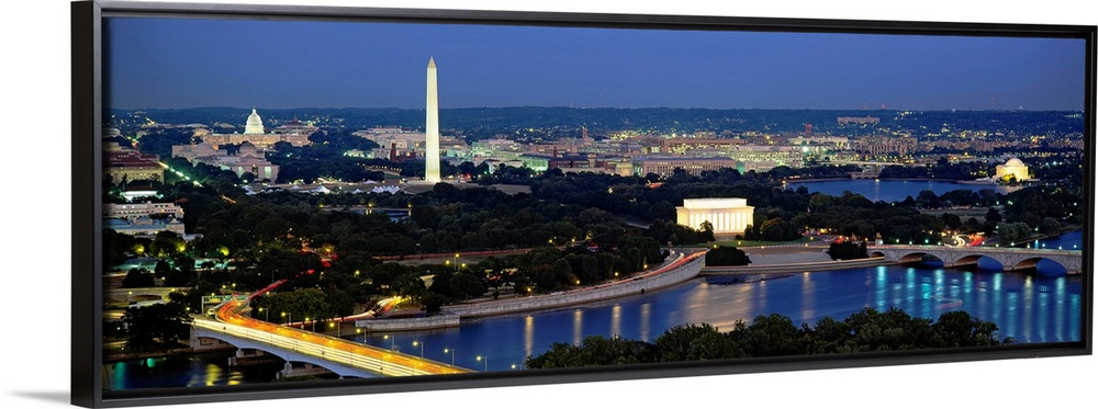 Panoramic photograph of the nation's capital at night with bright lights reflected in the water.  The Washington Monument ...