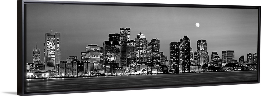 A panoramic of the skyscrapers in Boston lit up at night and the moon above the city.