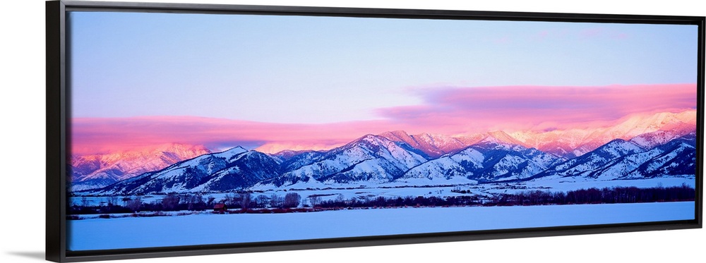 A panoramic snowscape photograph of plains and clouds passing over mountains at the end of the day.