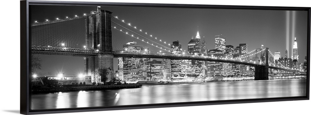 A panoramic landscape photo taken after 2001 of Manhattan and Brooklyn Bridge shining bright over the East River at night.