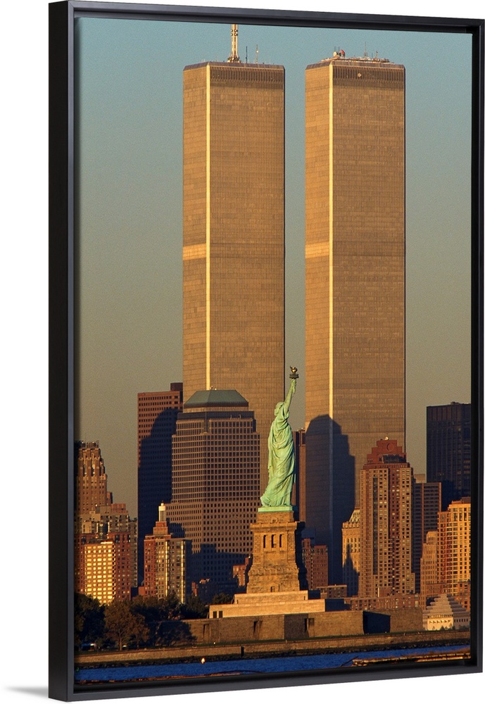 Vertical photograph of the World Trade Center towering over Manhattan with the Statue of Liberty in the foreground.