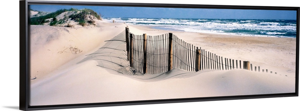 A wooden fence separates sand dunes from the Atlantic Ocean in this panoramic image.