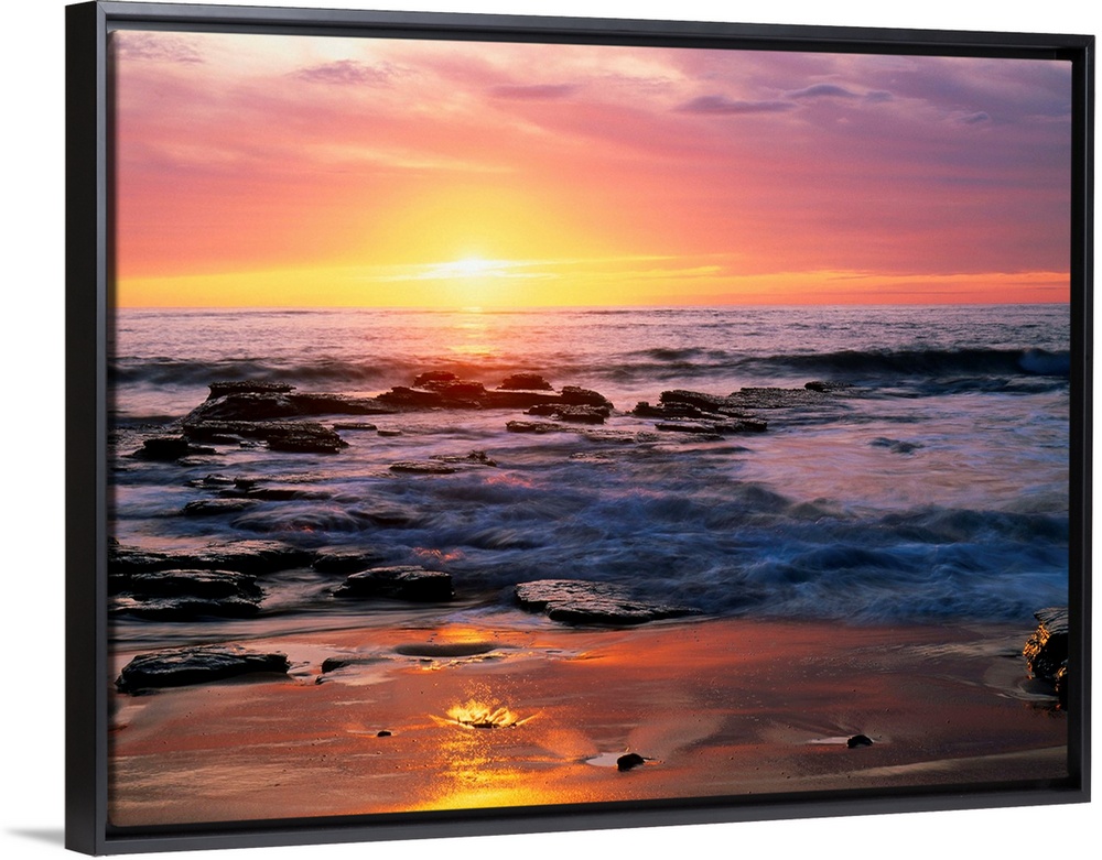 Photograph of rocky shoreline at sunset with a cloudy sky.