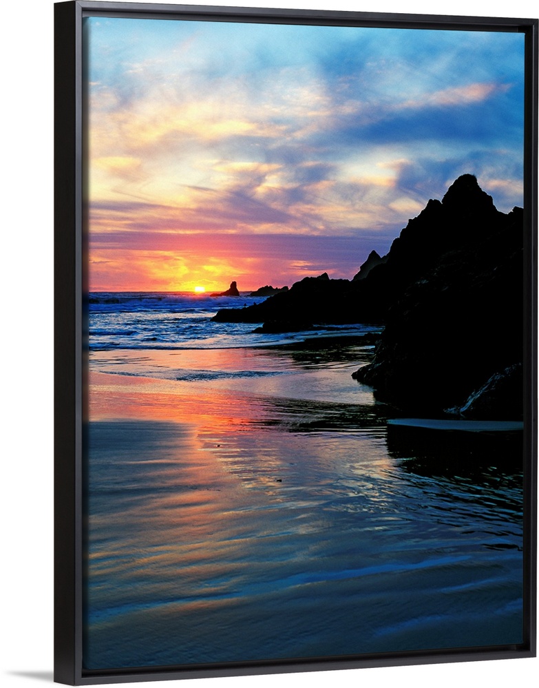 Sun below the horizon in a seascape with a rocky beach and waves.