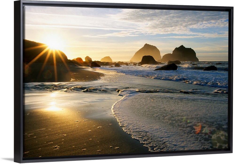 Panoramic photograph displaying a sunset over an ocean and sandy beach.  In the background you can see the waves hitting l...