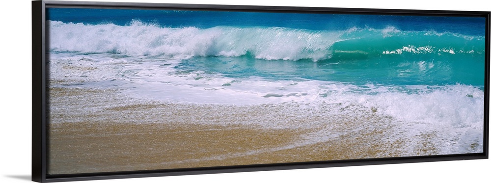 Panoramic photograph of water crashing onto the sand and being swept back out to sea.