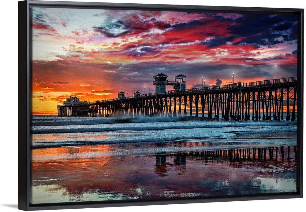 The Oceanside Pier is silhouetted as sunset turns the reflected clouds from yellow to pink to gun metal grey, and finally ...