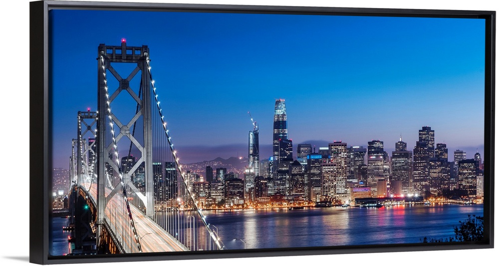 Photograph of the Bay Bridge and the San Francisco skyline lit up at dusk.