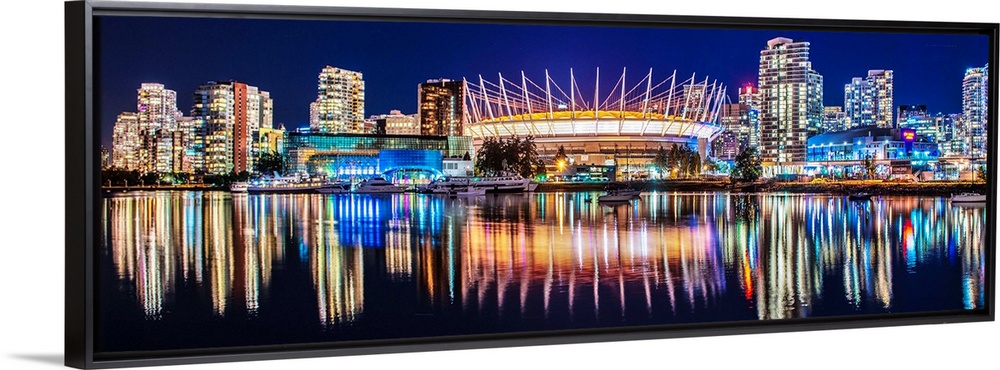 Panoramic photograph of BC Place Stadium and part of the Vancouver skyline lit up at night and reflecting onto the water, ...