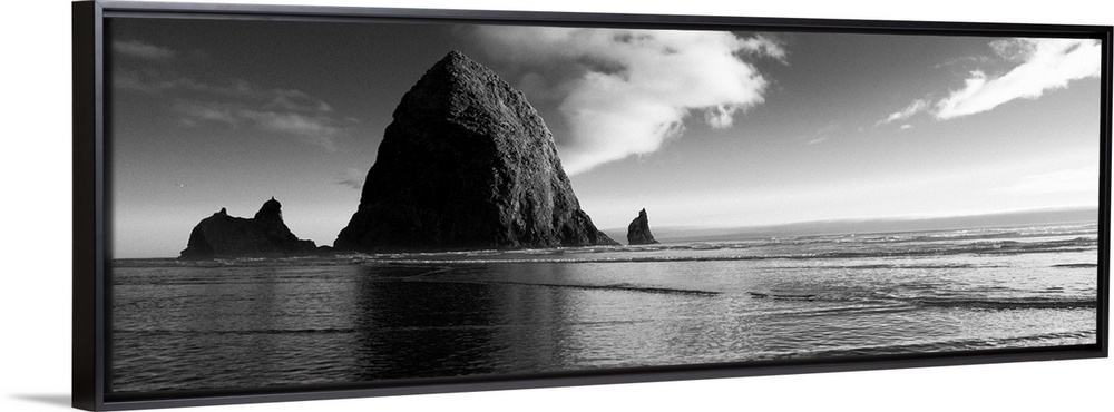 Black and white panoramic photograph of Haystack Rock with rippling waters.