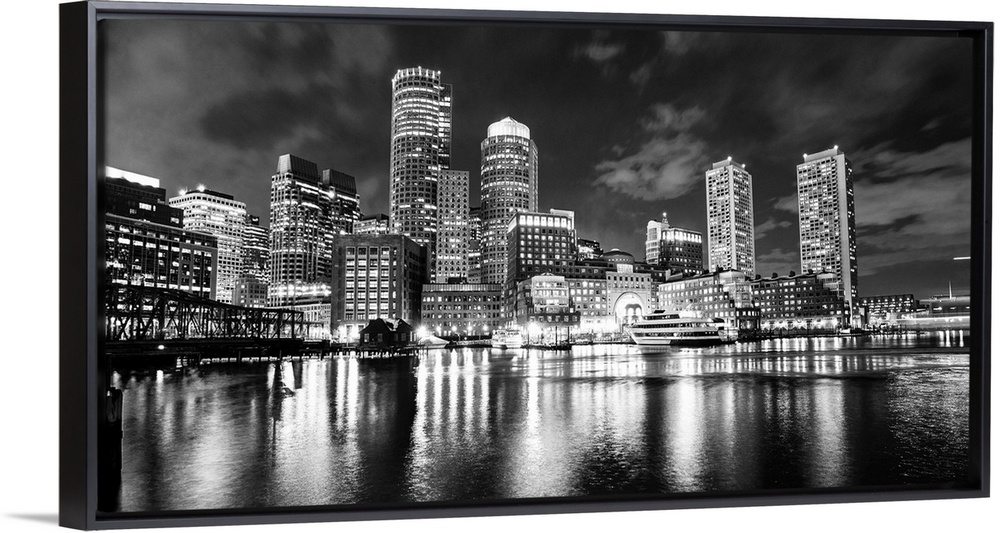 Panoramic view of the Boston City skyline at night, with lights reflected in the water.